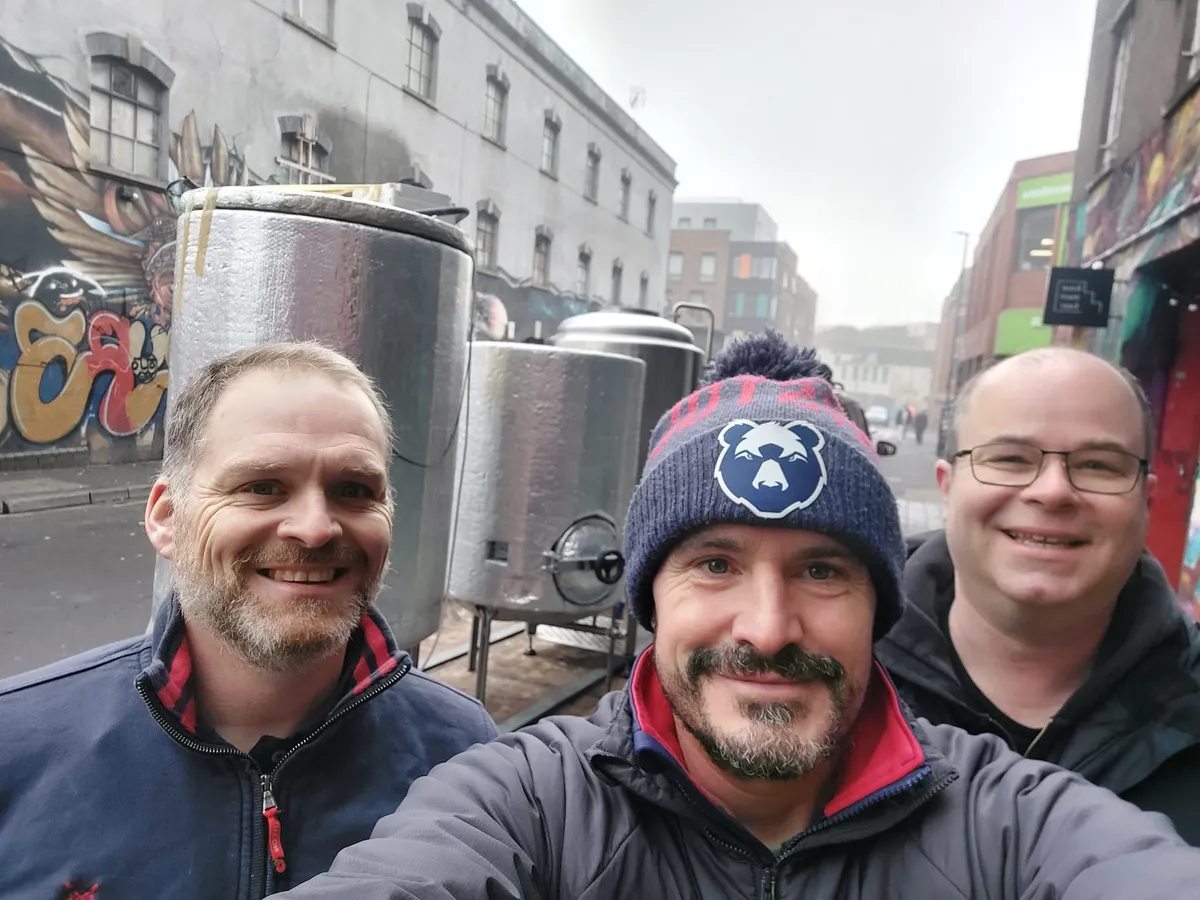 Simon, Sam and Craig standing in front of the stainless steel brew kit on a Bristol street